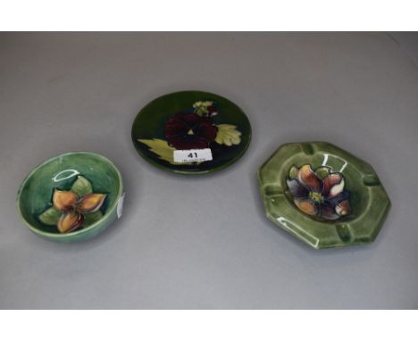 Three vintage pieces of Moorcroft all having green ground included are an ash tray, a pin dish with pansy to centre and anoth