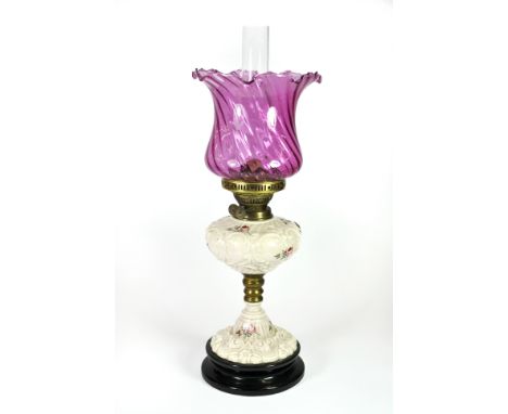 An Edwardian ceramic oil lamp with a cranberry glass shade, H. 57cm.