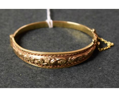 An Edwardian 9ct gold lady's hinged bangle, embossed with foliate scrolls, 15.4g