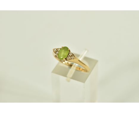 A 9CT GOLD GEM SET DRESS RING, centring on an oval cut green stone assessed as peridot, flanked within colourless circular cu