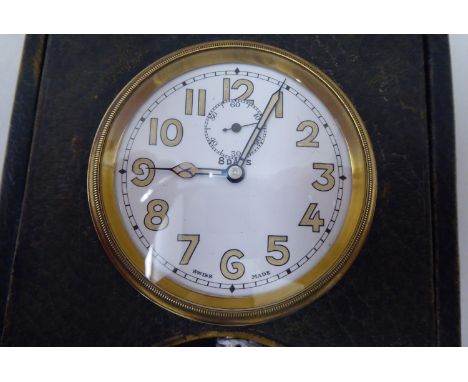 A vintage travel timepiece; the 8 day movement faced by a white enamel Arabic dial, in a stained green hide, folding case, on