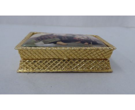 A gold plated pill box, the hinged lid set with an enamel tablet, depicting three children, playing 