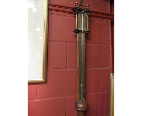 A George I walnut moulded veneered cistern barometer with stepped pediment top surmounted by three brass ball finials, brass 