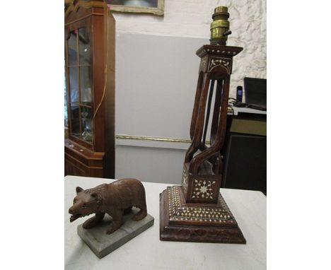 A Black Forest carved wooden bear mounted on a stone plinth and a Middle Eastern wooden table  lamp with inlaid bone decorati