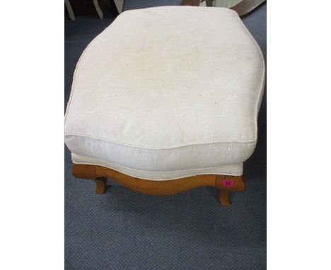 A modern overstuffed foot stool with cream upholstery above a beech frame