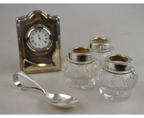 Three small cut glass jars with silver collars, London 1923, a silver-faced desk clock with easel stand and an infant's spoon