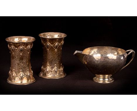 An Arts & Crafts silver milk jug of hammered design with foliate handle, James Aitchison, London 1908, 10.5cm wide and a pair