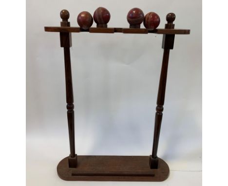 A hardwood cricket bat stand, on turned supports, to hold three bats, and with two cups for leather balls, 64 cm wide, and fo