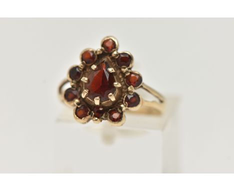 A 9CT GOLD GARNET CLUSTER RING, designed as a central pear shape garnet within a circular cut garnet surround, to the bifurca