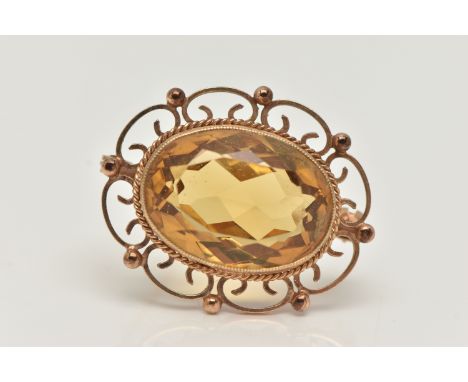 A 9CT GOLD CITRINE BROOCH, of an oval form, set with a large oval cut citrine, in a milgrain collet setting to the scrolling 