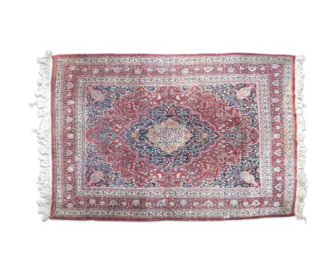A LARGE PERSIAN RED GROUND WOOL CARPETthe open centre field woven with a large cartouche medallion filled with scrolls and fl