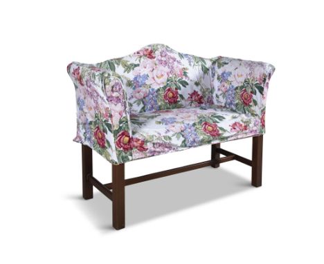 A MAHOGANY FRAMED HUMP BACK SETTEEwith out-scrolled arms and padded seat, upholstered in floral fabric, raised on square bloc