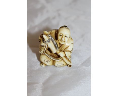 A Japanese carved ivory netsuke as a seated man with hobby horse, signed to base