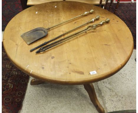 A circular pine breakfast table raised on a single pedestal to tripod base, two wrought iron fire dogs and three brass fire t