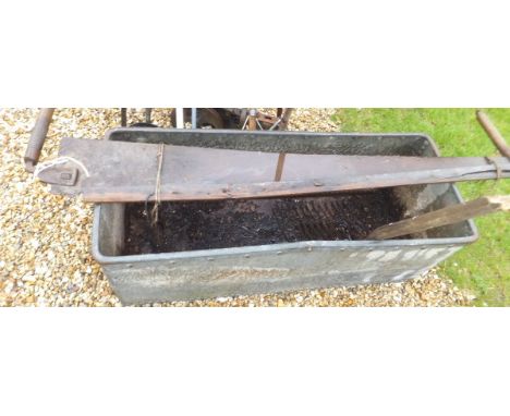 A two man cross cut saw, a large galvanised metal feeding trough and a hay fork
