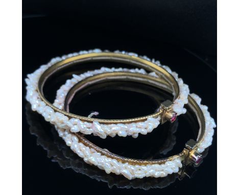 A PAIR OF FRESHWATER PEARL SPRUNG BANGLES. THE MULTI PEARL DESIGN WOVEN INTO THE REVERSE OF THE BANGLE, THE CLASP SET WITH A 