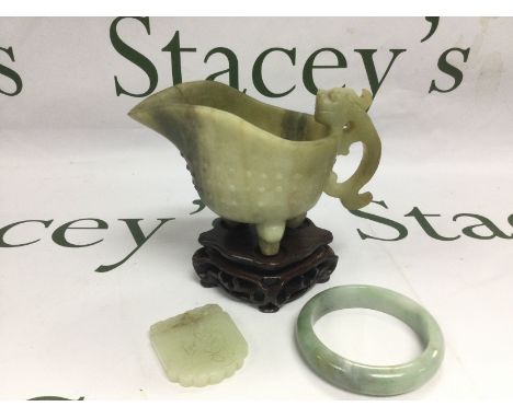 Three jade items comprising a carved jug, raised on a hardwood stand, a bangle etc. Shipping category D.