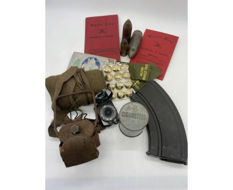A collection of war time memorabilia, a cigarette tin, a bike lamp, bullet heads, lapel bands, army service paperwork,  compa