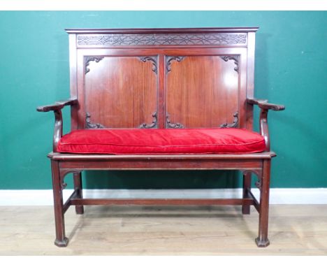 A Chippendale style mahogany settle with blind fret carved frieze, shaped arms and red cushioned seat, raised on squared supp