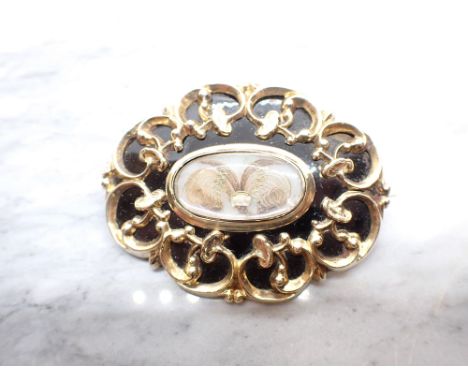 A Victorian Mourning Brooch with central oval hair picture within black enamel and gold frame, inscriptions in memory of four