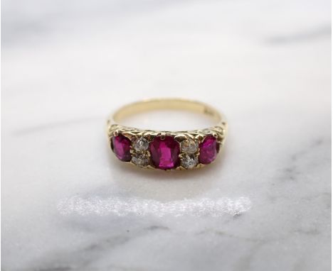 A Ruby and Diamond Ring pavé-set three graduated oval-cut rubies interspersed with pairs of old-cut diamonds, stamped 18ct, r