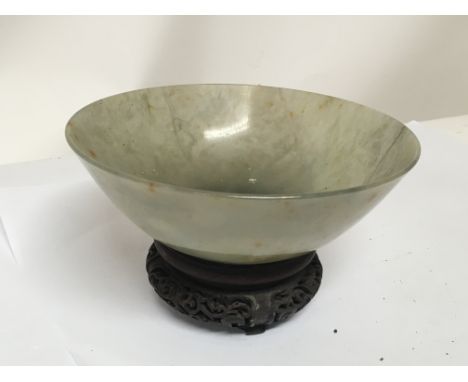 A 19th century Chinese green jade bowl with a carved hardwood stand. The bowl with stress cracks possible natural rather than