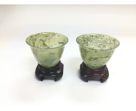 A par of jade cups on hardwood stands, total approx height 6.5cm. Shipping category D.