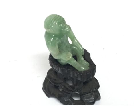 A small Chinese carved green jade monkey on a hardwood base. Height including stand 5cm