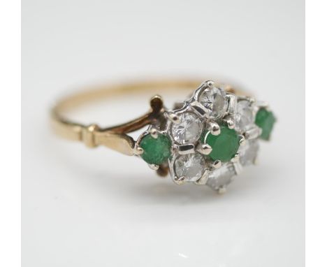 A vintage diamond, emerald and 9 carat gold floral cluster ring. Set with three round mixed cut emeralds in open back claw se