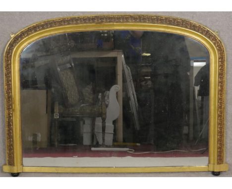 A Victorian gilt overmantel mirror with arched plate and gesso floral decoration on porcelain bun feet. H.80 W.110cm 