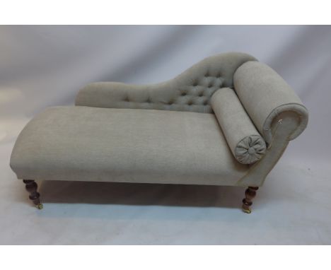 A contemporary chaise lounge with button back stone linen upholstery raised on turned mahogany legs and castors