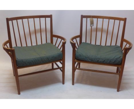 A pair of 1970's teak stick back armchairs with rush seats and raised on tapered legs jointed by stretchers