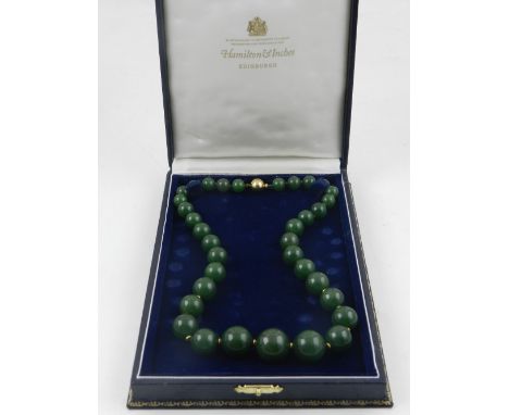 A Chinese green jade necklace, the graduated beads of rounded form, having yellow metal placers and yellow metal ball clasp, 