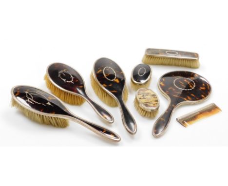 A George V silver and tortoiseshell backed dressing table set, comprising three hand brushes, hand mirror, small brush, a cre