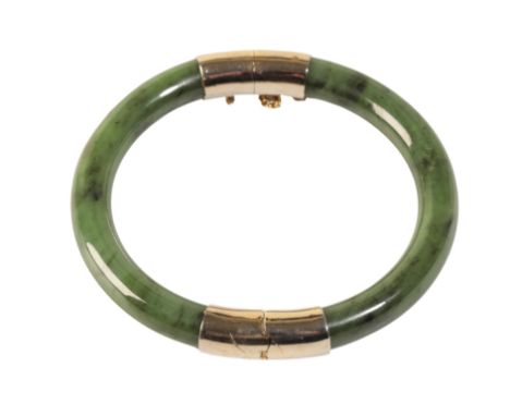 A JADEITE HINGED BANGLE, with unmarked yellow metal mounts and safety chain
