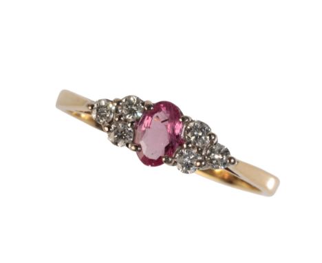 A RUBY AND DIAMOND CLUSTER RING, the central oval cut pale pink ruby flanked by a cluster of three diamonds on either side,on