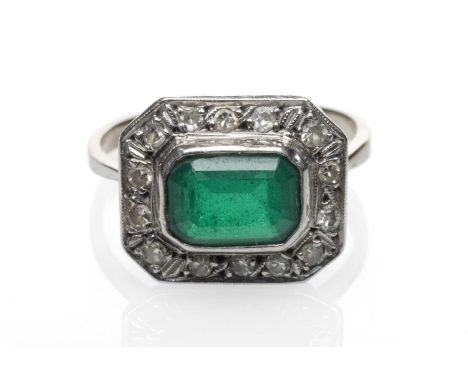 WHITE METAL EMERALD & DIAMOND CHIP CLUSTER RING, the central emerald (8 x 6mms) within a border of fourteen diamond chips, ri