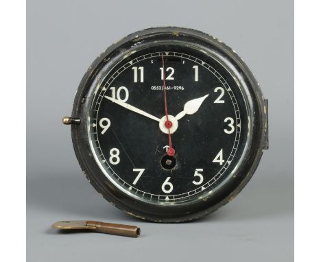 A British Royal Navy mechanical bulkhead clock with black dial and broad arrow mark. Numbered 0552/461/9296. Diameter of dial