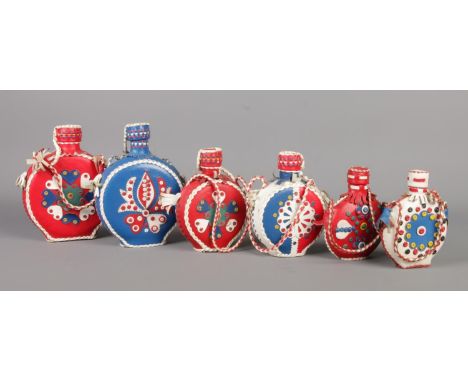 A set of six vintage Folk Art leather-covered flasks, featuring rustic, colourful leather with floral designs and twisted wov