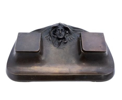 A Jugendstil bronze ink stand, in the Art Nouveau style, cast with womans head with flowing hair, between two plain inkwells,