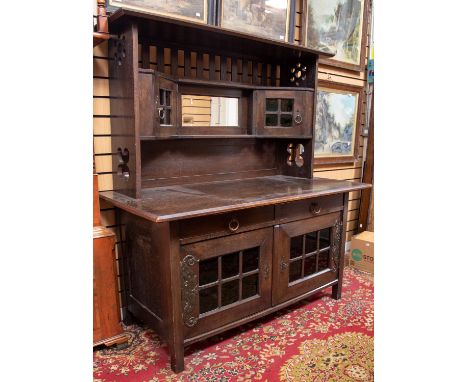 An Arts and Crafts oak sideboard, circa 1900, the base with two drawers over to leaded and glazed cupboards, below an overhan