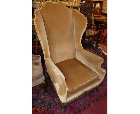 An early 20th century wing back scroll armchair, pale Dralon fabric upholstered with squab cushion, raised on floral relief c