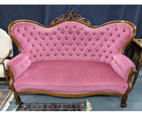 A Victorian mahogany pink button back upholstered sofa, ornately carved crest rail with grapes flanked by C-scrolls and leave