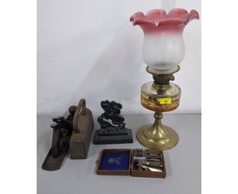 An oil lamp with a frosted and cranberry coloured shade, a wooden smoothing plane, a 16kg weight, a small door porter, and a 