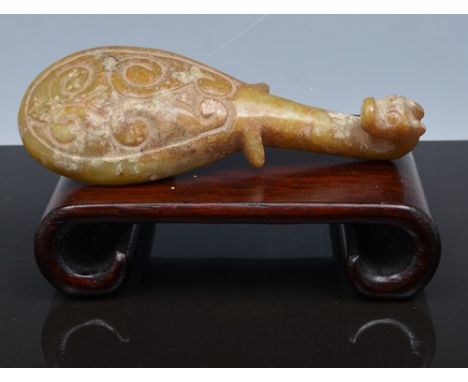 A Chinese carved hard stone buckle, Yuan style, in greenish amber tones,with a dragon mask, broad bodied, 10.5cm, on a wooden