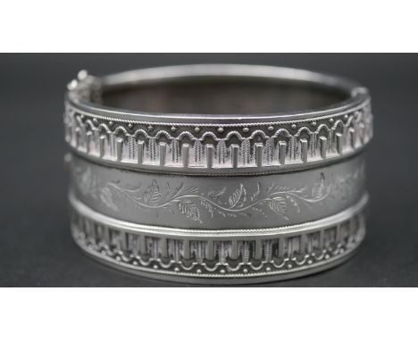 A Victorian engraved white metal cuff bangle with wirework detailing and foliate garland design. It has a push catch with saf