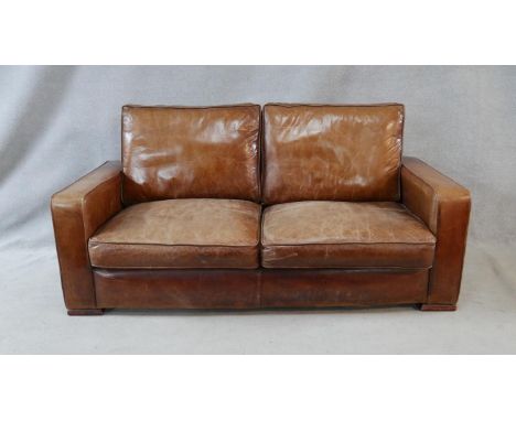 A contemporary vintage style sofa in tan leather upholstery on block platform supports. H.75 W.183 D.90cm 