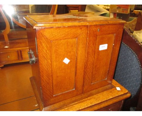 Early 20th Century oak smokers cabinet with two panel doors enclosing a fitted interior with silver mounted Doulton tobacco j