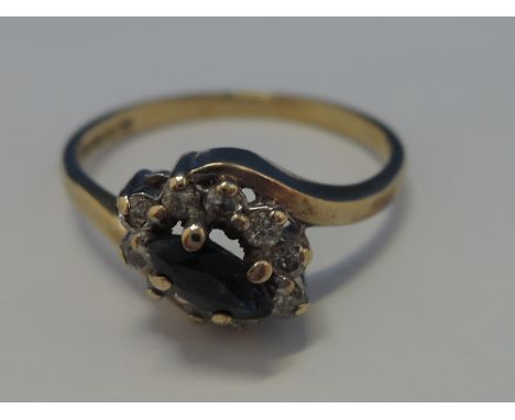 A ladies dress ring having an oval sapphire within a diamond chip surround with crossover shoulders on a 9ct gold loop