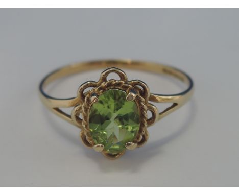 A ladies dress ring having an oval peridot within a frilled mount on a 9ct gold loop